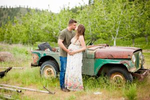couple kissing in front of vintage vehicle with orchard behind