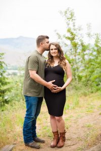 man in green shirt kissing temple of pregnant wife in black dress