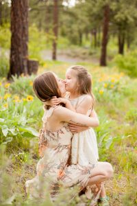 mother kneeling and kissing daughter in white dress