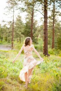 woman holding dress and twirling in wooded area with bed of wildflowers