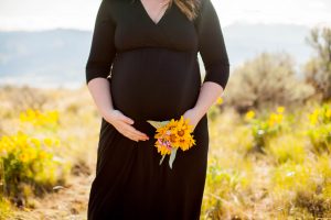 close up of pregnant mother wearing black dress holding bouquet of yellow flowers