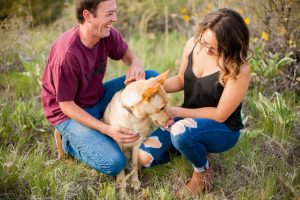 couple petting their yellow dog between them and laughing