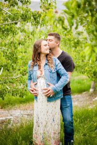 man holding pregnant wife from behind and kissing her temple